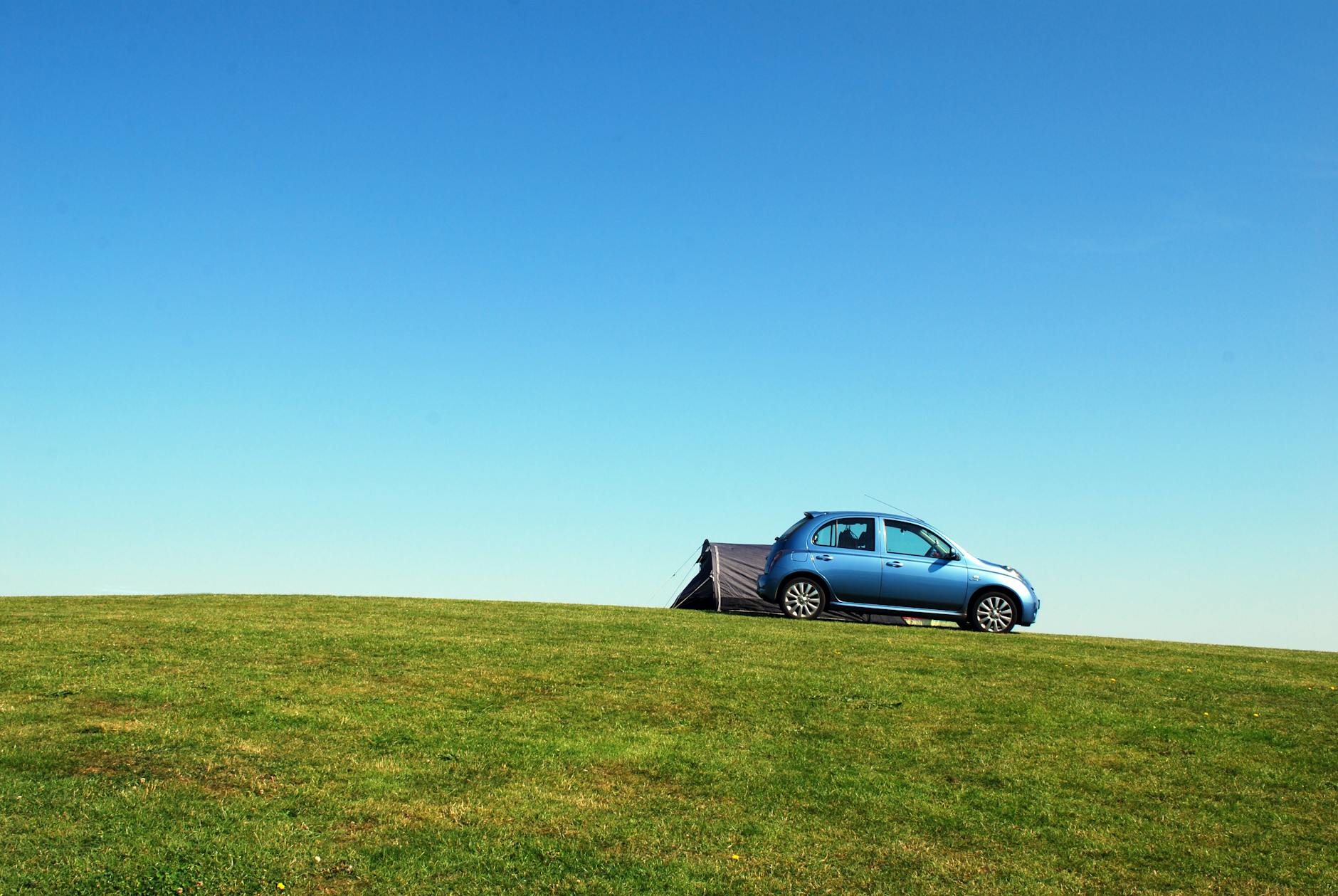 blue hatchback on green grass field under blue sky